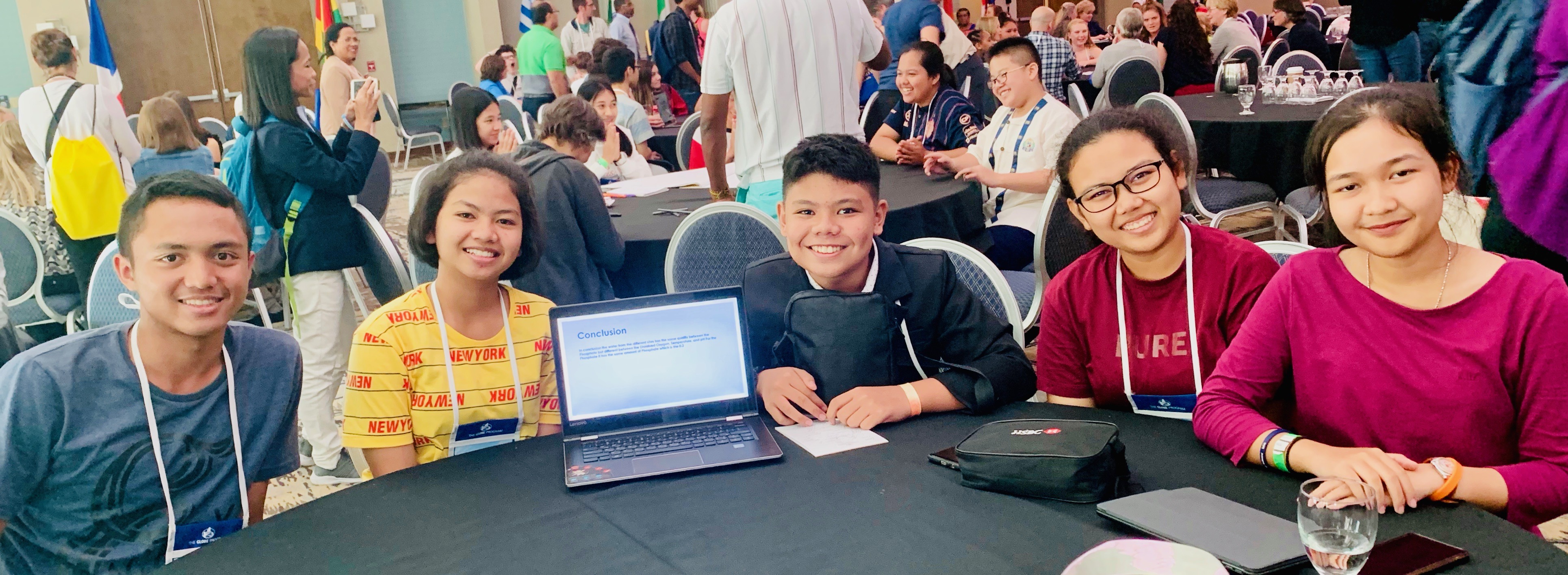 Five students sitting at a table, next to a laptop showing their project, at a GLOBE conference.