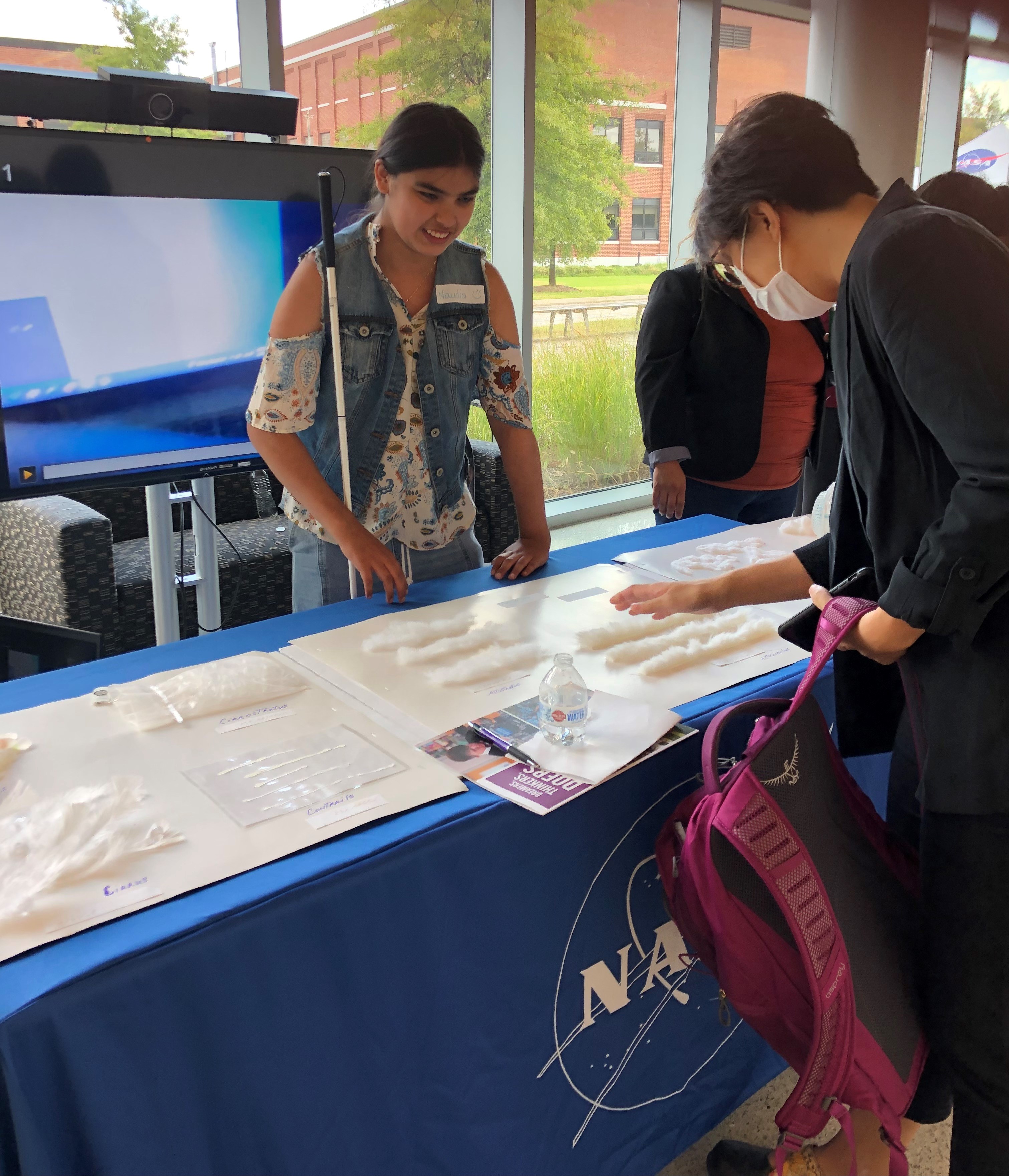 Three students looking at a table with 3-d cloud models. One student has a vision impairment and is using a white cane.