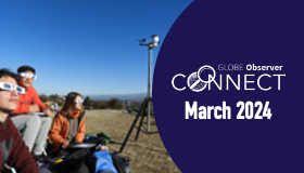 Three people with solar viewing glasses look up at the sky, with portable weather station to the side.