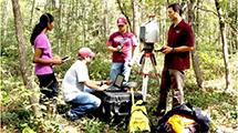 Four researchers in a forest surrounded by a collection of research equipment.