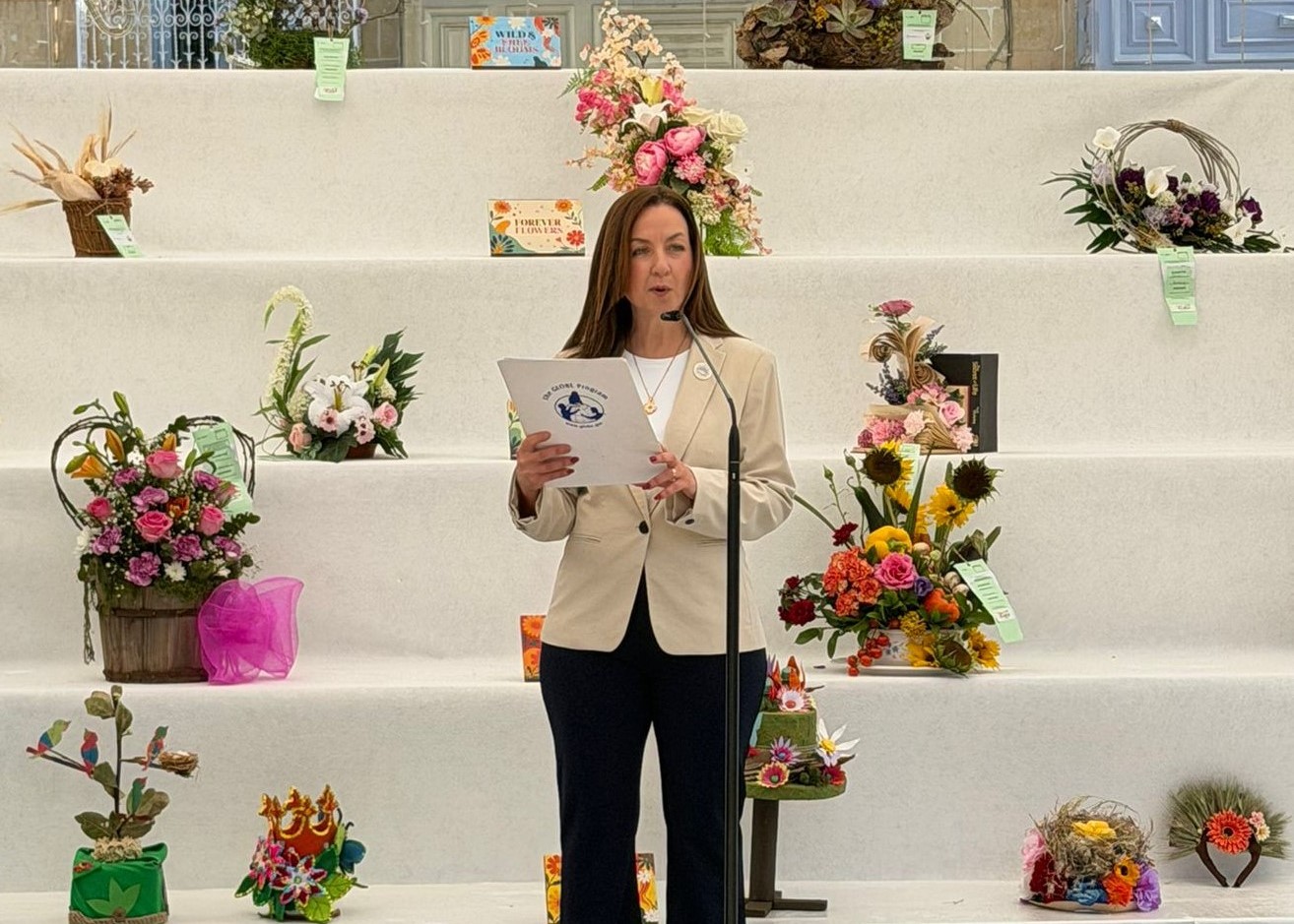 Person talking into microphone in front of a display of flowers.