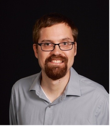 Brad Hegyi, wearing glasses and a gray shirt, smiling at the camera.