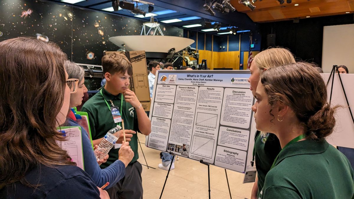 three students present their research poster to two STEM reviewers