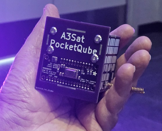 A person holds an A3Sat PocketQube small satellite in the palm of their hand