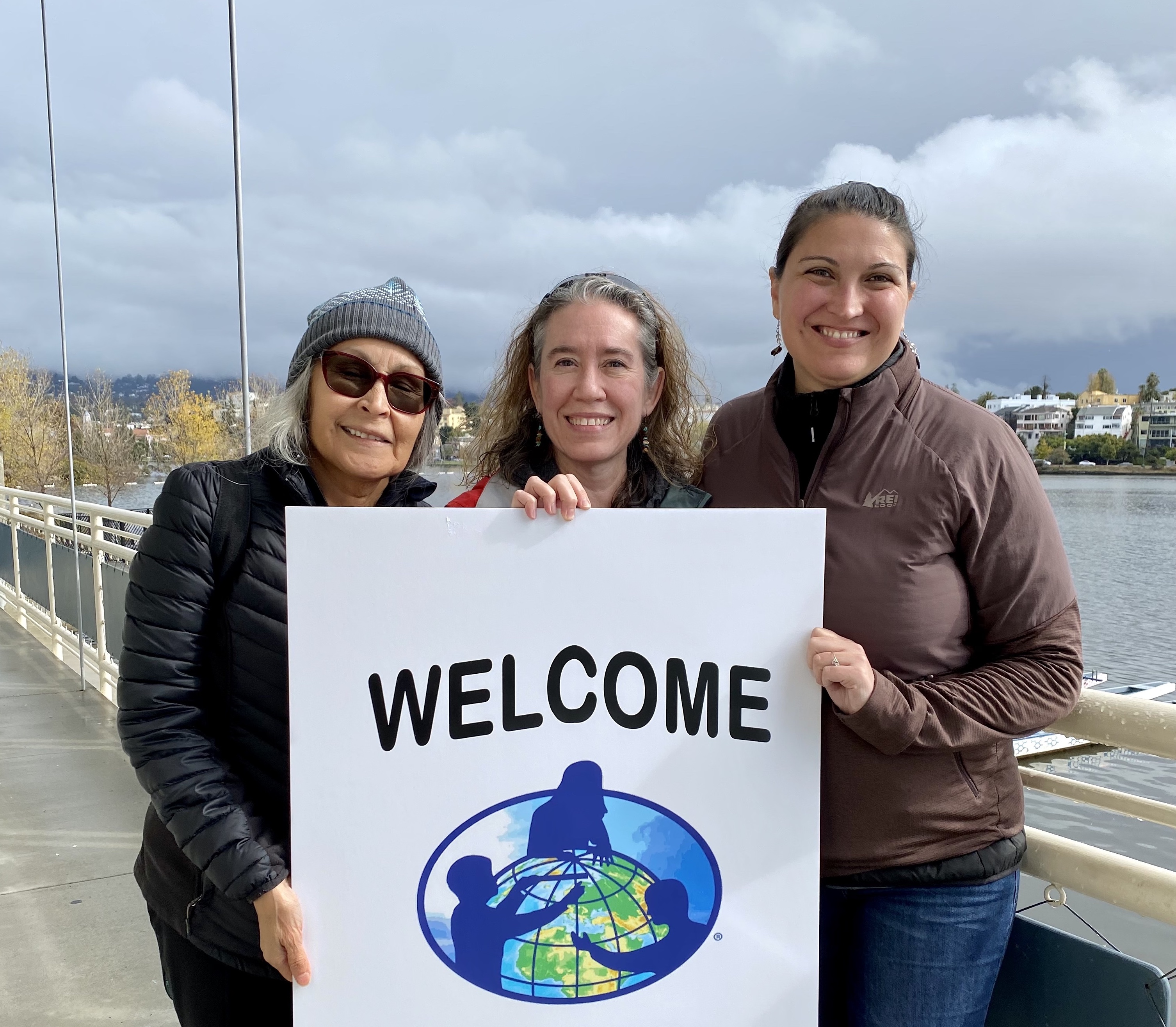Three GLOBE Partners hold a welcome sign with the GLOBE logo
