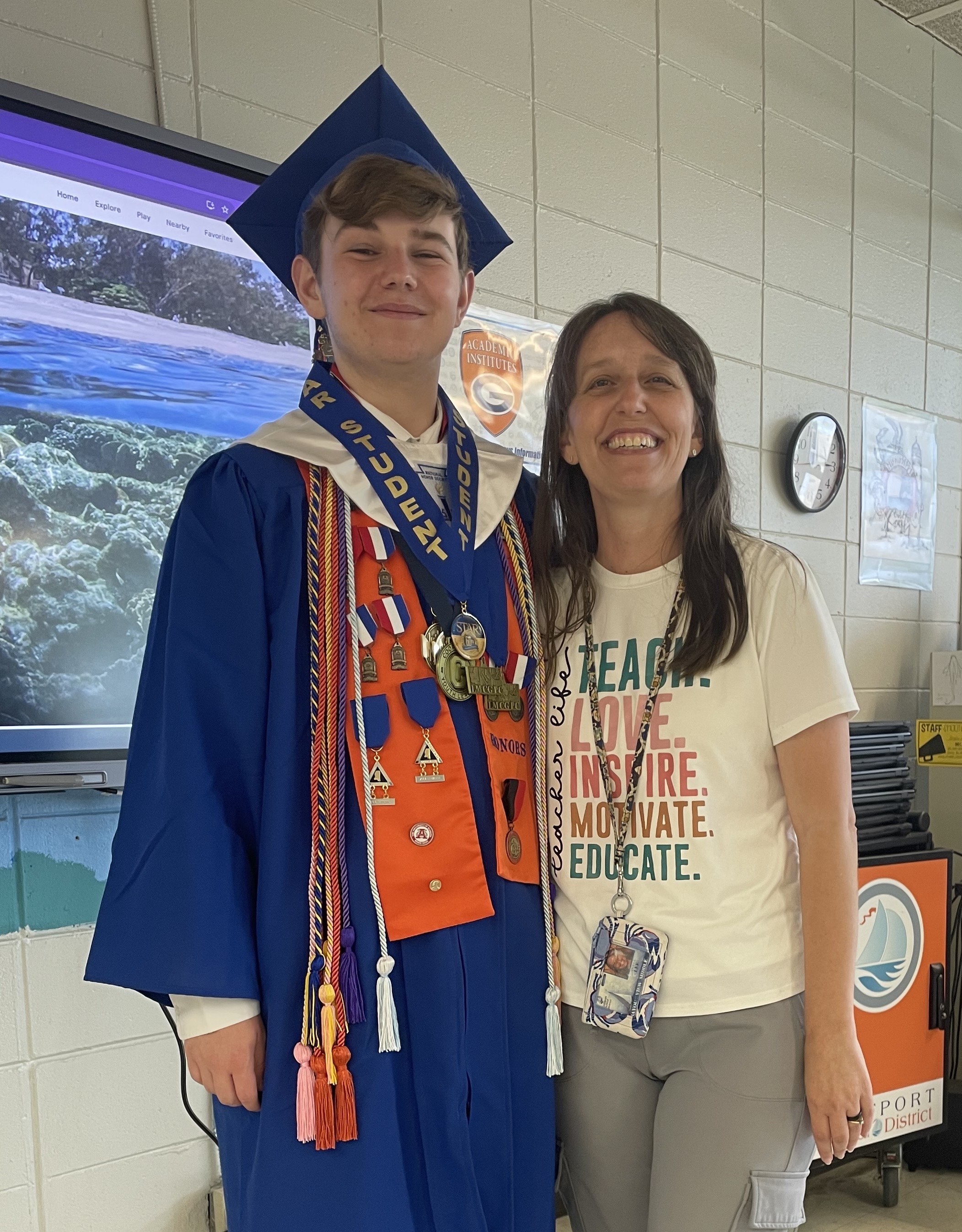 GLOBE student Jackson P., in his graduation gown with medals and cords around his neck, stands beside his middle school teacher Mrs. Angela Lee