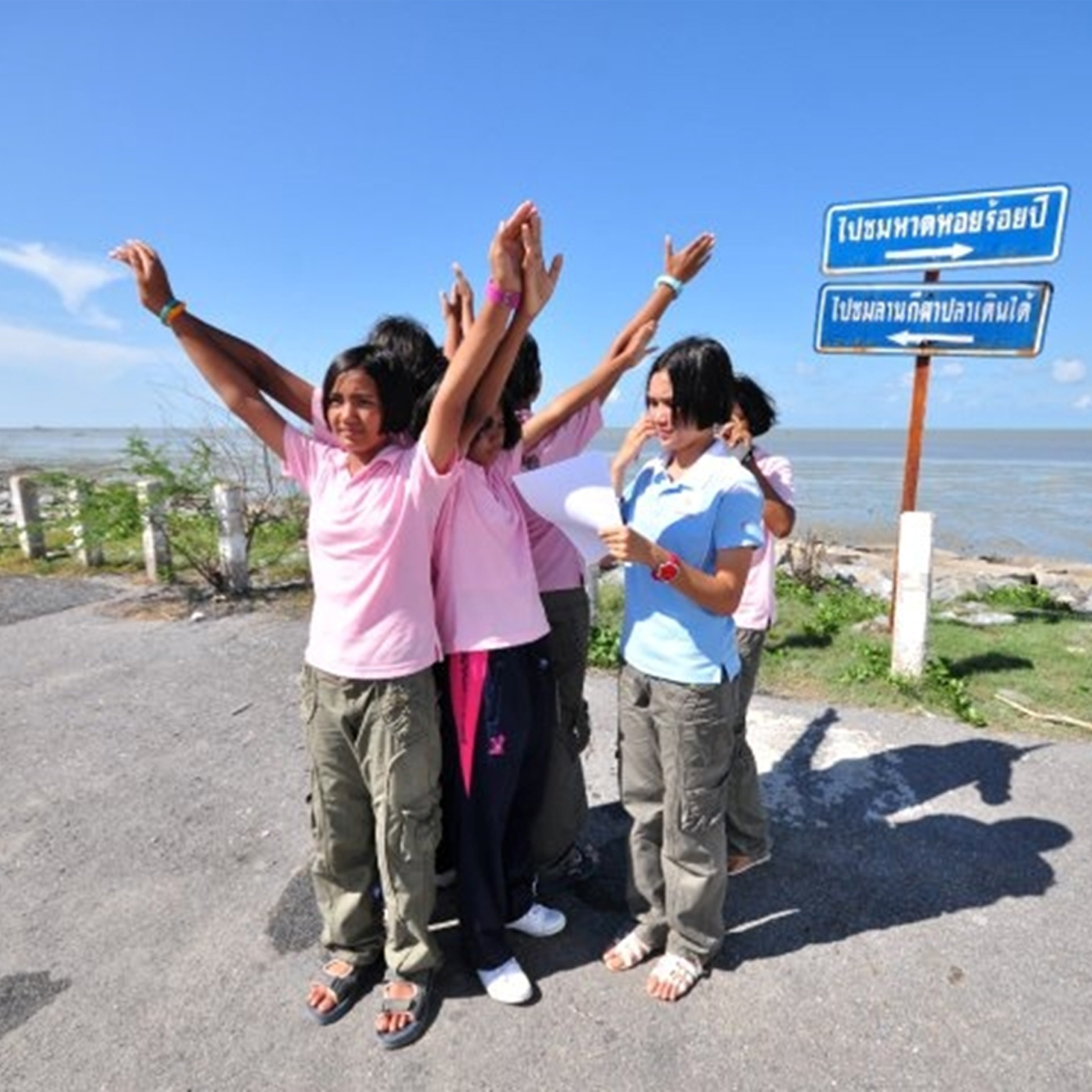 Five students stand together outside with their hands raised above their heads in a v-shape.