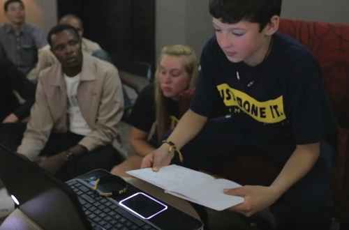 A group of students watch a boy present finding to other students online.