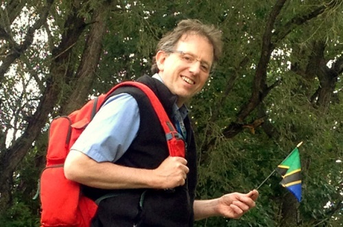 A man stands holding a backpack and flag.