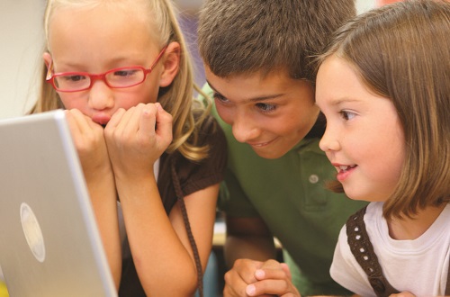 Three students look together at a computer screen.