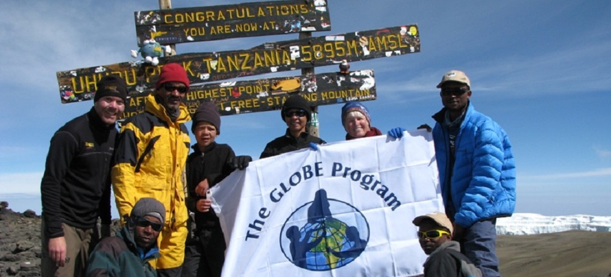 A group of people stand in front of Kilimanjaro's summit sign.