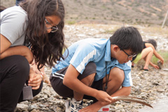 Two students take a close look at the soil and water nearby.