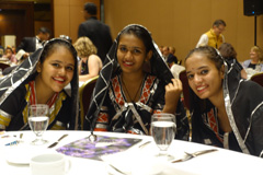 Three young women sit at a banquet table in traditional dress.