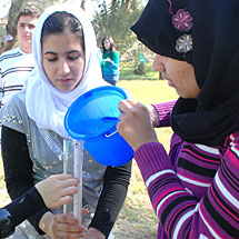 Students pouring water from a bucket into a tube.