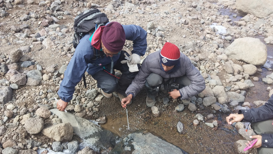 Three people take water samples from a brook.