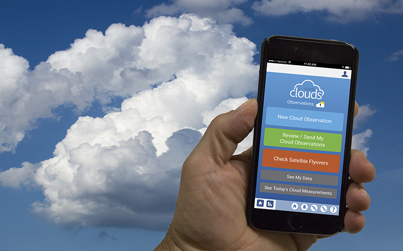 A hand holds a mobile device with puffy clouds in the background.