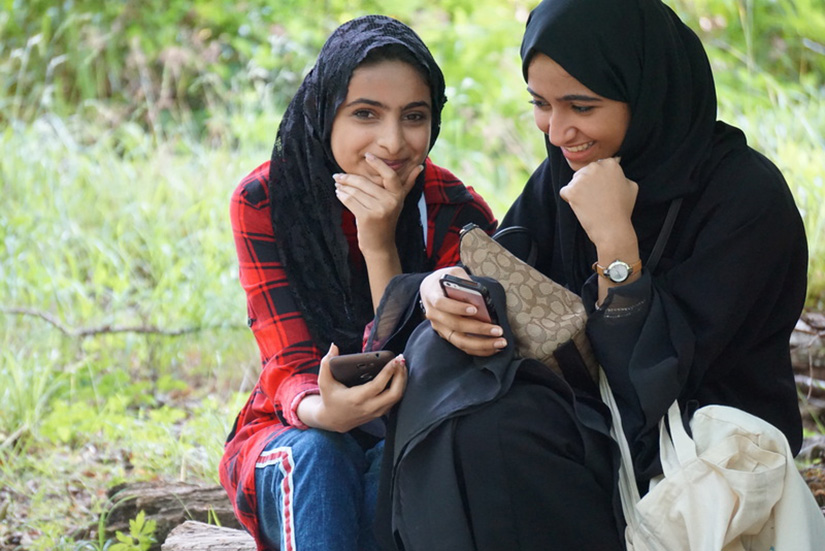 Two girls smile and hold their smart phones.