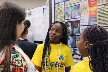 Two girls explain their science poster to onlookers.