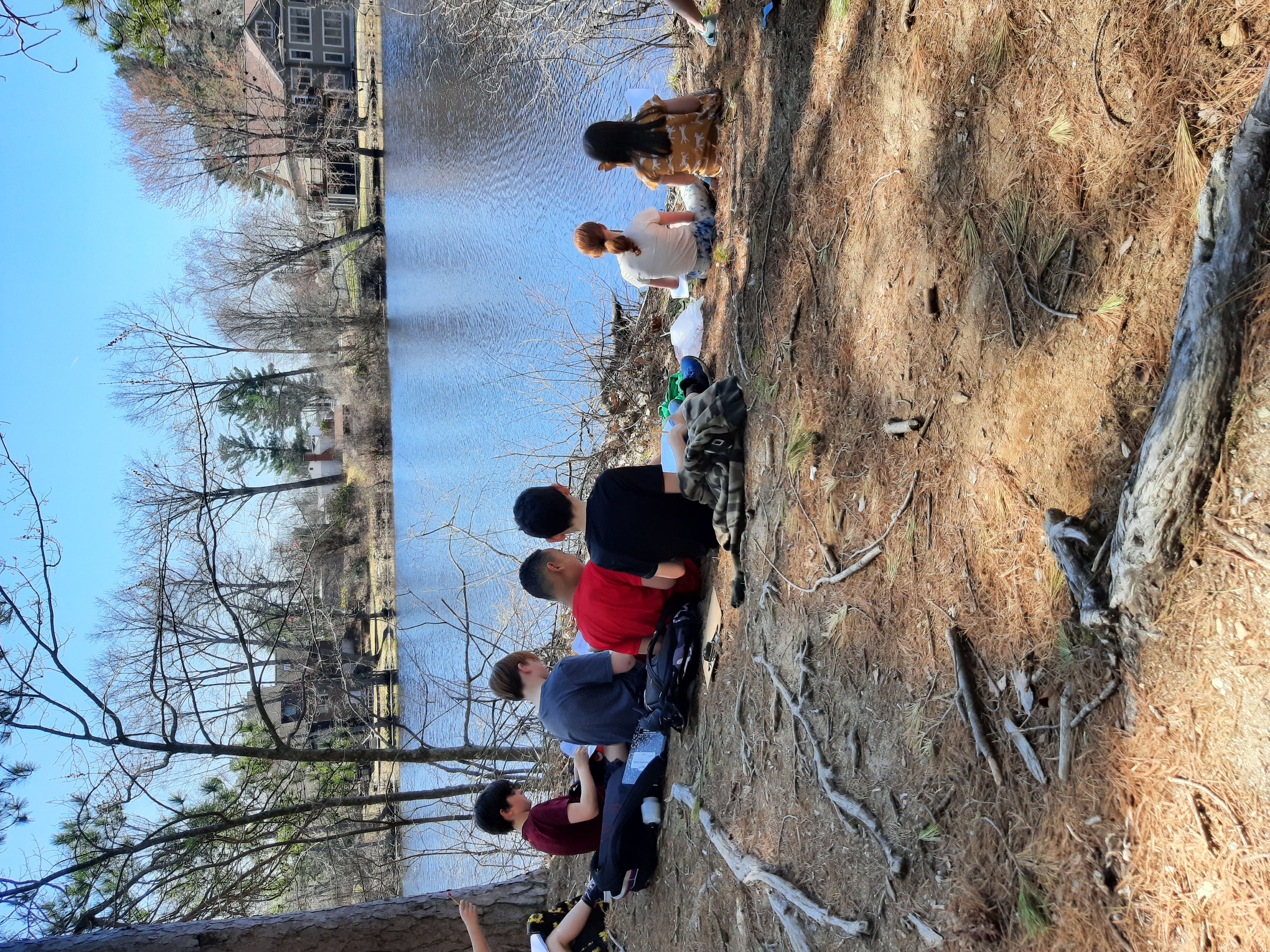 students sit on the bank of the Cocheco River to sketch the surrounding area