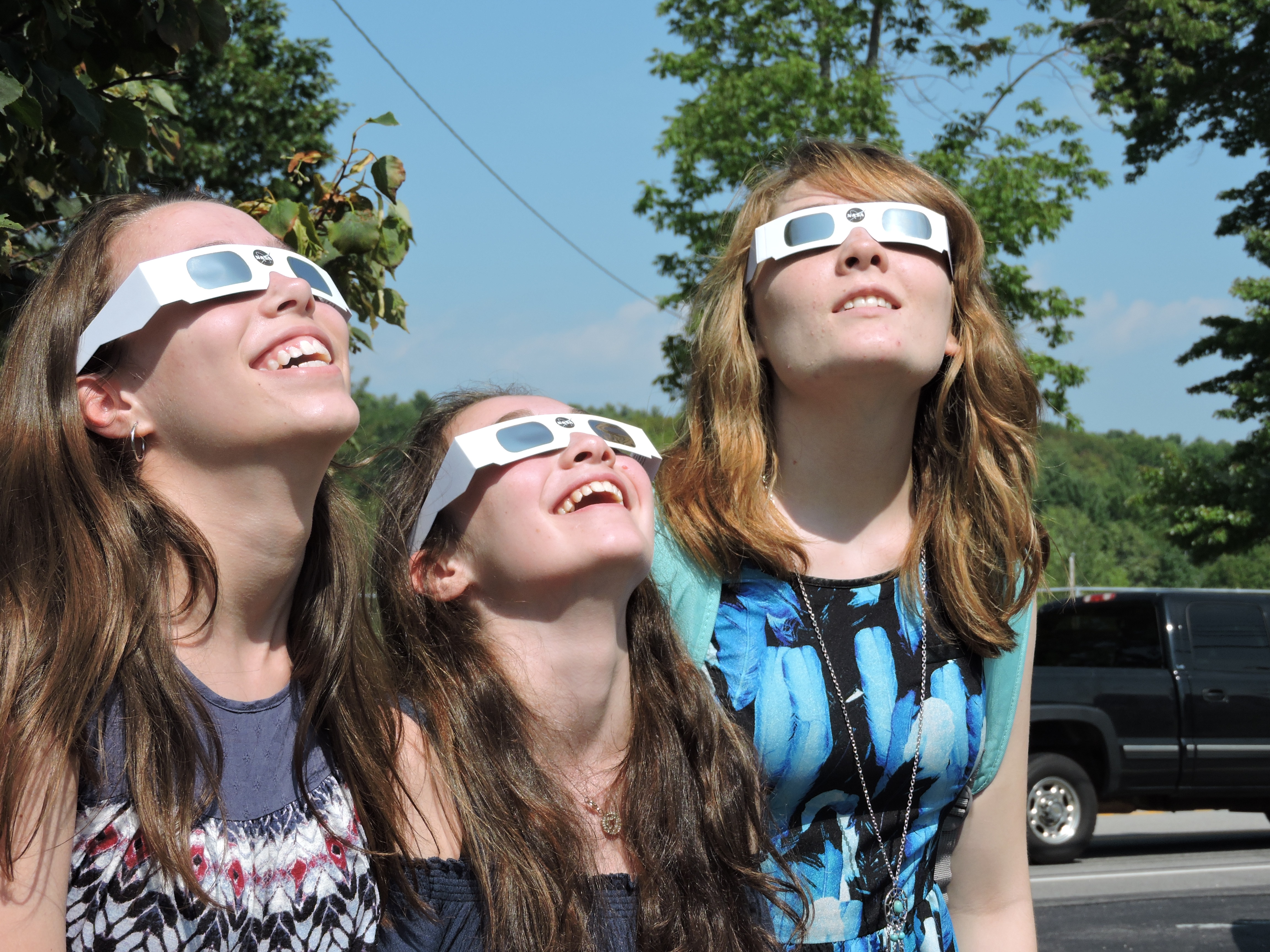 three young female students looking up through eclipse glasses smiling