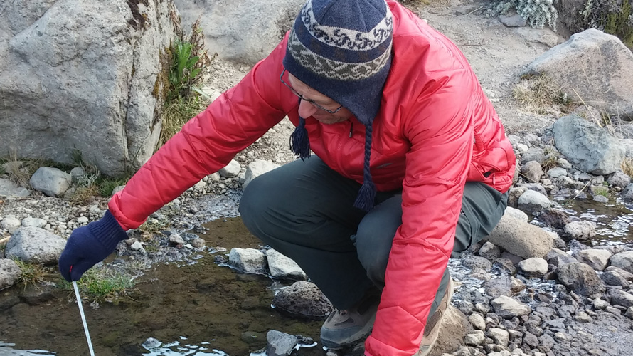 A man takes the temperature of water in a brook.